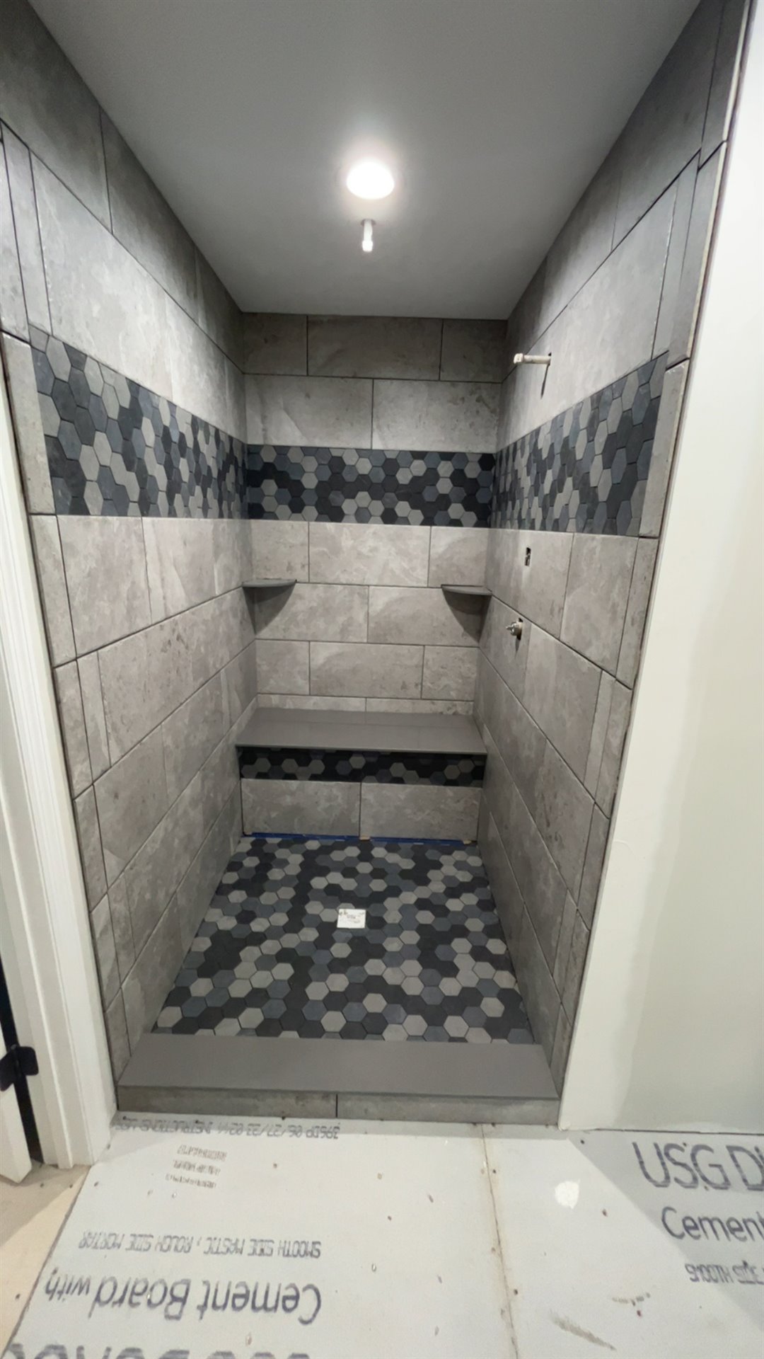 Custom gray tile shower with a patterned accent band, built-in bench, and matching floor