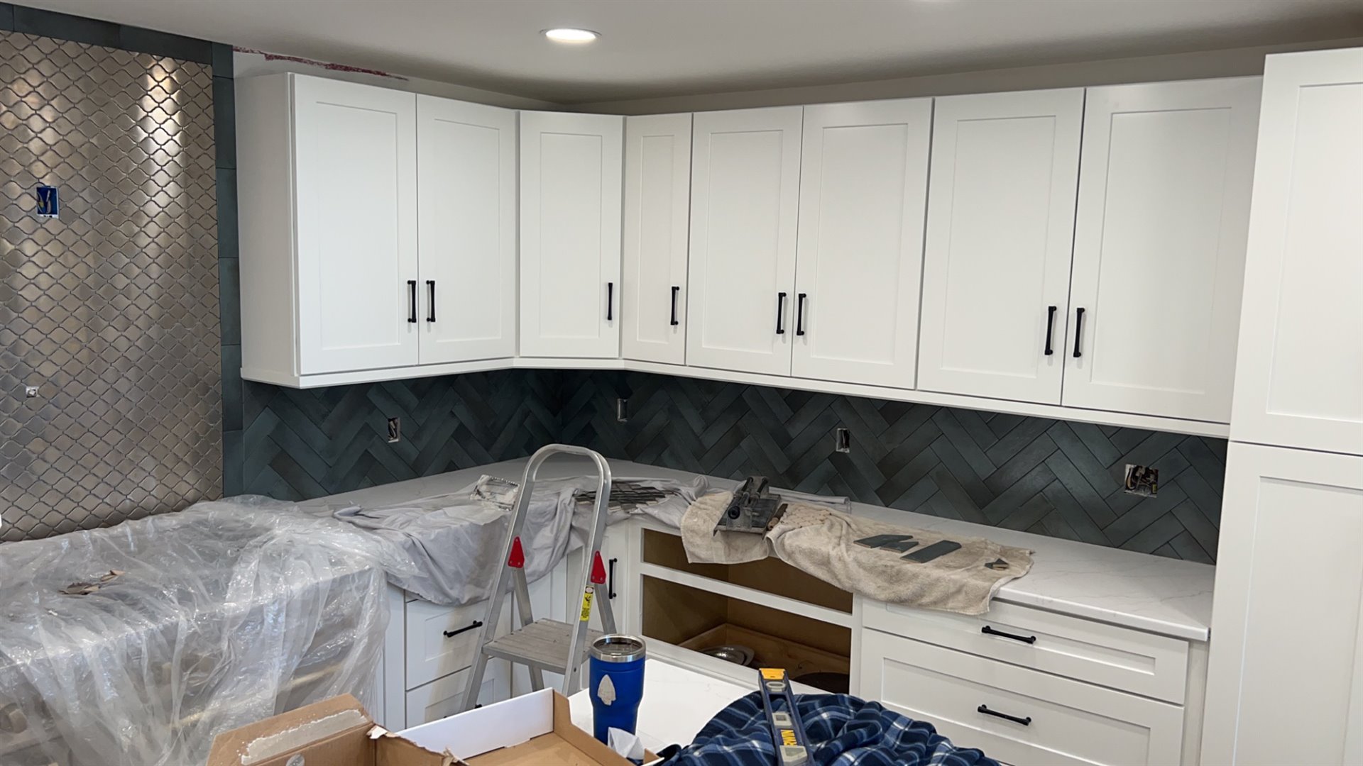 White kitchen cabinetry above a dark herringbone tile backsplash